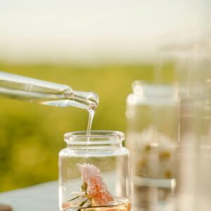 Close-up of a pipette adding liquid to a jar with a flower, outdoors in daylight.