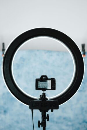 Shining round shaped lamp with photo camera on tripod taking picture of blue paper in studio