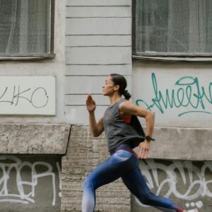 A woman in activewear jogging swiftly past a graffitied wall in an urban setting.