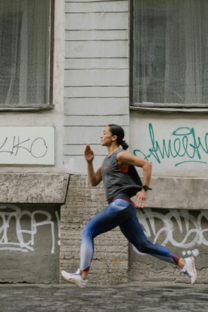 A woman in activewear jogging swiftly past a graffitied wall in an urban setting.