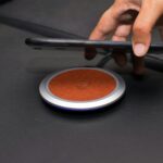 Close-up of a hand placing a smartphone on a wireless charging pad on a leather surface.