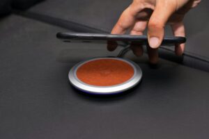 Close-up of a hand placing a smartphone on a wireless charging pad on a leather surface.