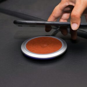 Close-up of a hand placing a smartphone on a wireless charging pad on a leather surface.